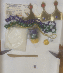 KingKingCakes.com king cake displayed with DIY decorating supplies and Mardi Gras extras. 
