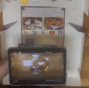  KKC king cake brochure beside a phone showing online decorating instructions reached through a QR code.