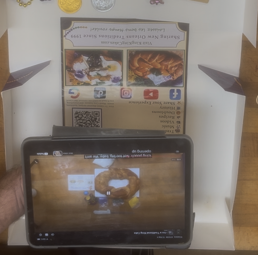 KingKingCakes.com king cake brochure beside a phone showing decorating and Mardi Gras content reached through a QR code.